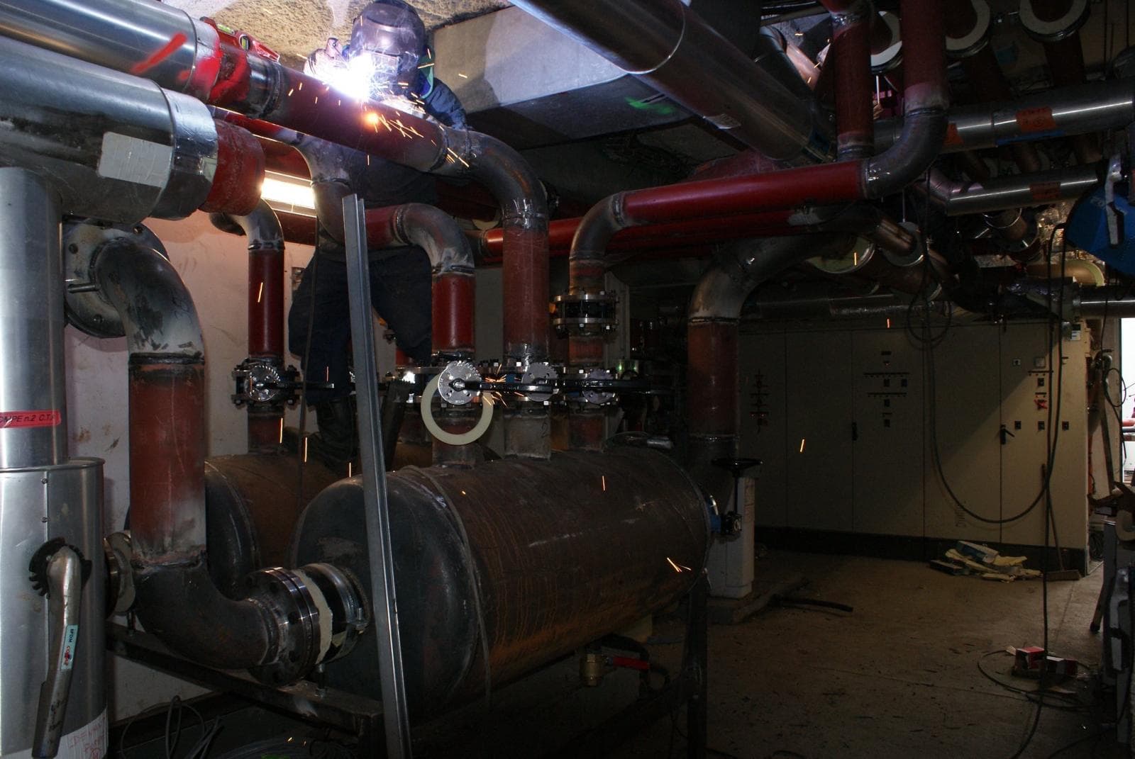 Soudeur au travail sur réseau de tuyaux en chaufferie de grand immeuble